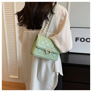 Quilted mint green shoulder bag with pearl chain strap worn by a model in a studio setting