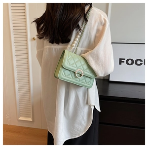 Detail of mint green quilted bag with pearl ring closure and chain strap on model