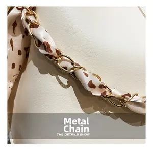 Macro view of gold chain hardware intertwined with leopard print silk scarf on bag