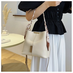 Detail of cream bucket bag featuring silk scarf wrapped handle and gold chain accents