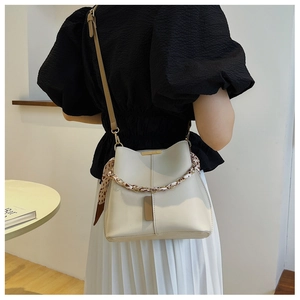 Model wearing a minimalist cream bucket bag with metal chain and decorative silk scarf