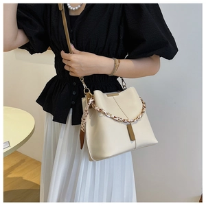 Detailed view of off-white bucket bag with decorative silk scarf chain on a model