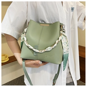 Detail of light green bucket bag featuring floral scarf wrapped handle and gold chain