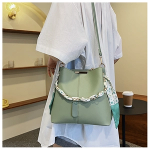 Detail of green leather bucket bag featuring a decorative floral silk scarf on the handle