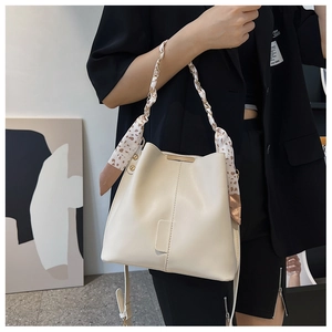 Detail of off-white bucket bag featuring silk scarf wrapped handle and metal chain accent