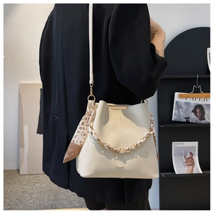 Fashionable beige bucket bag with metal chain scarf handle shown on model's shoulder