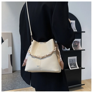 Detail of cream bucket bag featuring a silk scarf woven chain strap and smooth texture