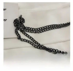 Close-up of sleek black metal chain hardware for shoulder bag over white fabric