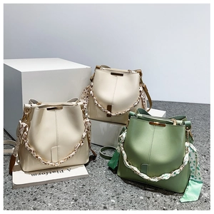 Close-up of PU leather bucket bag featuring silk scarf handle and golden chain detail