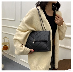 Close-up of black quilted shoulder bag with V-shaped stitching and chain strap on model