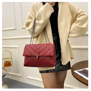 Detail of red V-quilted shoulder bag with silver metal buckle and chain strap on model