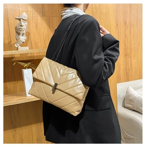 Quilted khaki crossbody bag with black chain strap shown on a model in a modern style