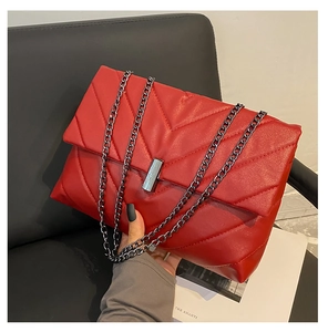 Detail of red quilted shoulder bag with V-pattern stitching and silver metal buckle closure