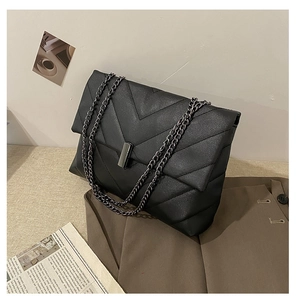 Detail of black chevron quilted shoulder bag with metal chain strap and rectangle buckle