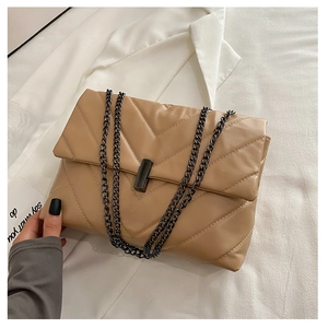 Macro shot showing khaki quilted chain bag with V-pattern stitching on soft white fabric