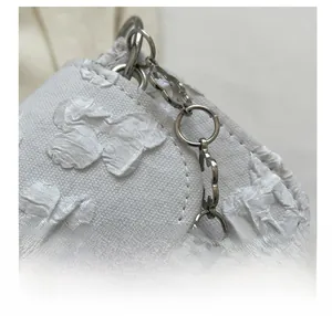 Detail of white textured fabric with floral embroidery and floral metal chain
