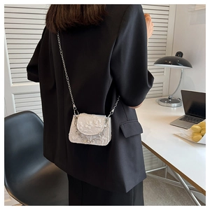 Mini white jacquard chain bag worn by model over a black blazer in a modern office