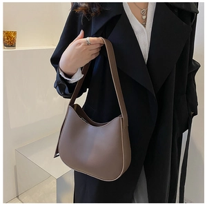 Brown semi-circle underarm bag in matte synthetic leather styled on a female model