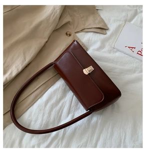 Close-up of chocolate brown glossy leather shoulder bag with gold metal press buckle lock