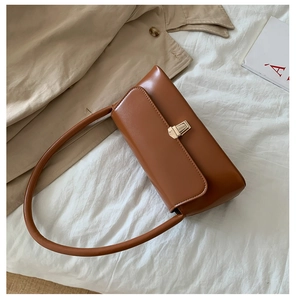 Detail of a brown leather baguette bag with golden rotating metal clasp on stylish background