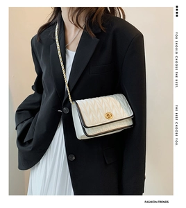 Detail of white leather crossbody bag with V-quilt stitching and gold turn-lock closure