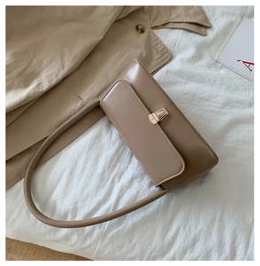 Close-up of a glossy beige baguette bag with a gold metal clasp on a textured fabric