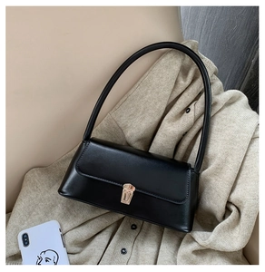 Detail of vintage black leather baguette bag with gold buckle on beige knitwear