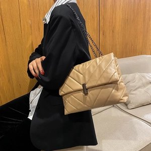 Chic quilted beige shoulder bag with metal chain strap worn on a black blazer