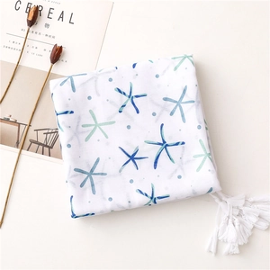 Detail of white cotton scarf featuring blue starfish prints and soft white fringe tassels