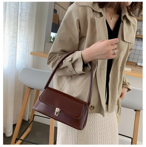 Close-up of a reddish-brown leather baguette bag with a gold buckle and slim shoulder strap