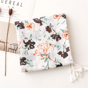 Détail d'une écharpe blanche avec motif floral à l'encre et franges souples