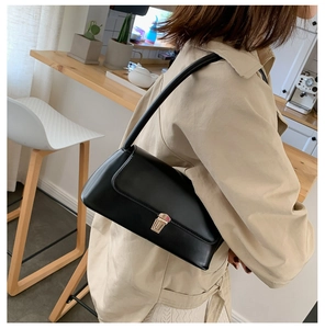 Detail of black leather bag with gold buckle shown on shoulder in a warm cafe