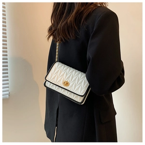 Close-up of white quilted crossbody bag with black trim and gold chain shoulder strap