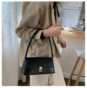 Close-up of minimalist black baguette bag with gold metal buckle on khaki trench coat