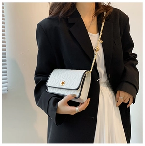 Close-up of white quilted crossbody bag with gold chain strap worn on black suit