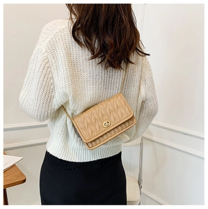 Beige quilted chain crossbody bag shown on a model wearing a white knit sweater