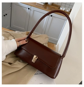 Close-up of a dark brown matte leather baguette bag with a gold rectangular metal lock