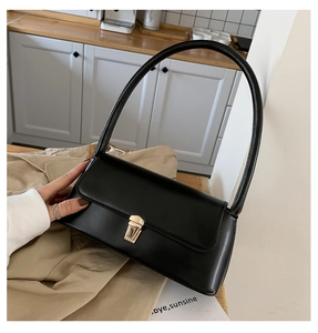 Close-up of black leather baguette bag with golden rectangular twist lock and slim strap