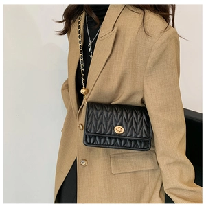 Detail of black quilted crossbody bag with golden twist lock and chain strap on model