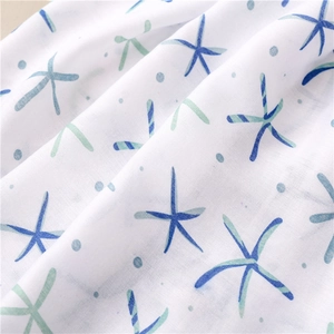 Detail shot of soft white cotton scarf featuring blue starfish prints and fringe texture