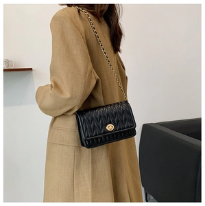 Detail of black quilted leather shoulder bag with gold twist lock on a beige trench coat