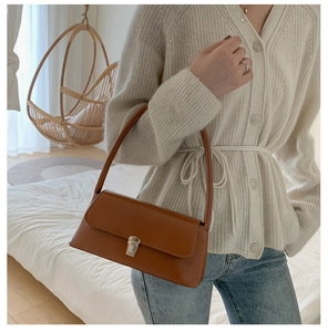 Detail of vintage brown leather baguette bag with silver buckle in a cozy indoor setting