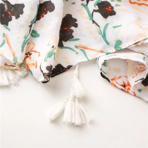 Détails du motif floral rétro et des pompons blancs sur une écharpe en lin souple