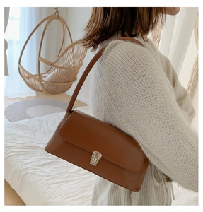 Close-up of a brown leather baguette bag with a silver buckle worn over the shoulder