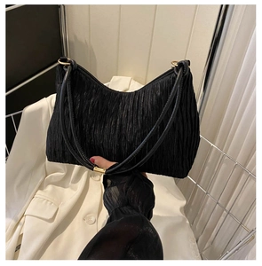 Detail of black pleated fabric underarm bag featuring glossy texture and golden metal rings