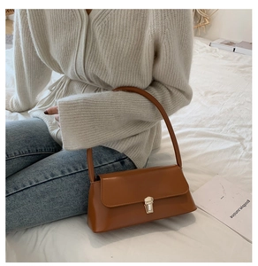Detail of a brown leather shoulder bag with silver buckle held by a model on a bed