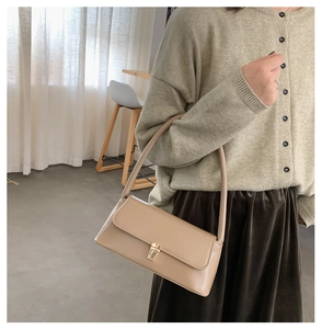 Detail of a beige baguette bag with matte leather and golden clasp on a model