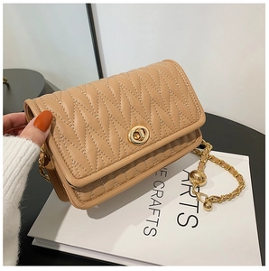 Detail of beige quilted crossbody bag with gold chain strap and metal ball ornament