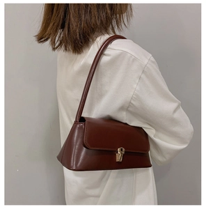 Detail of a brown leather baguette bag featuring a stylish gold metal magnetic snap closure