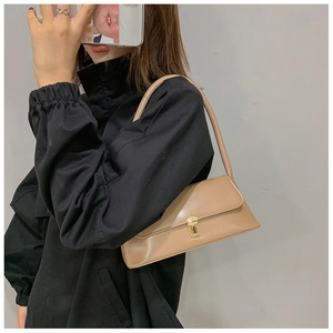 Fashionable beige leather baguette bag shown as a shoulder bag on a model's outfit
